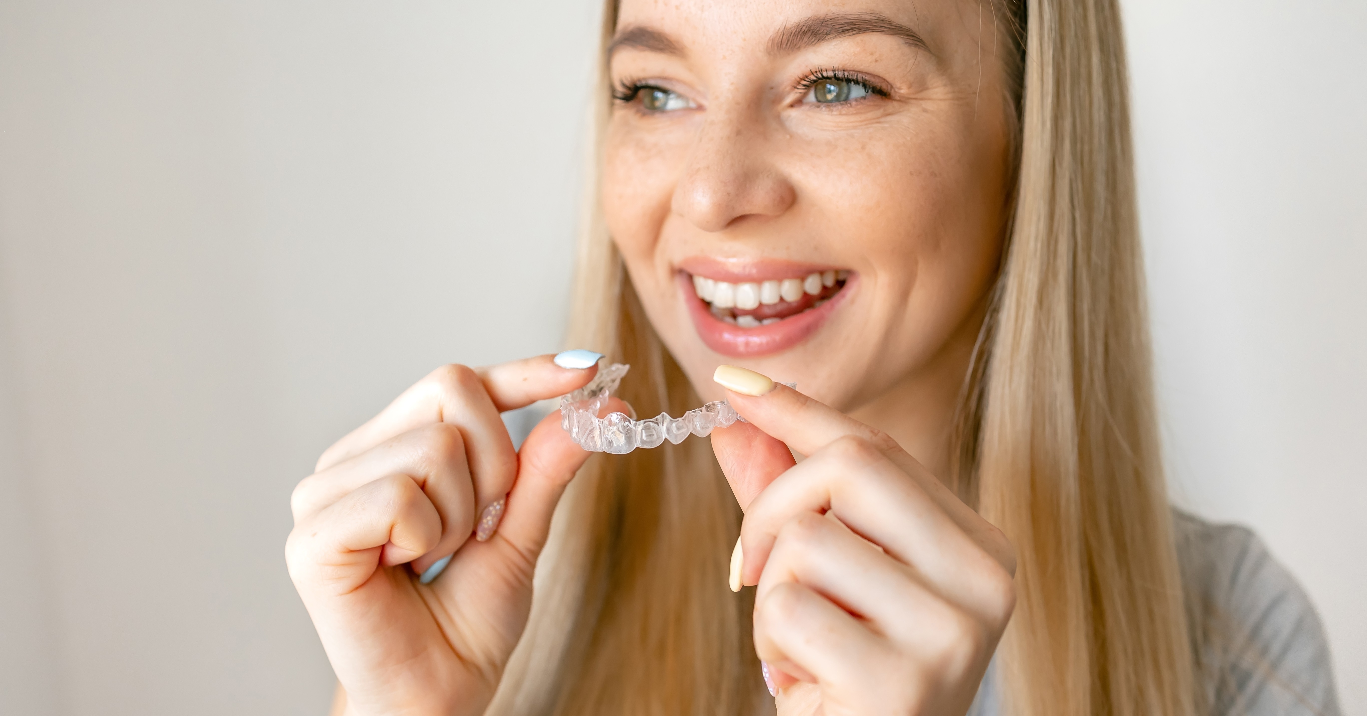 Pessoa sorrindo enquanto segura um alinhador transparente